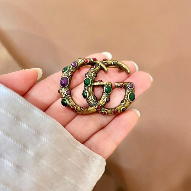 GUCCI 26S INTERLOCKING G MULTICOLOR GEM LOGO BROOCH IN ANTIQUE GOLD TONE METAL 625634